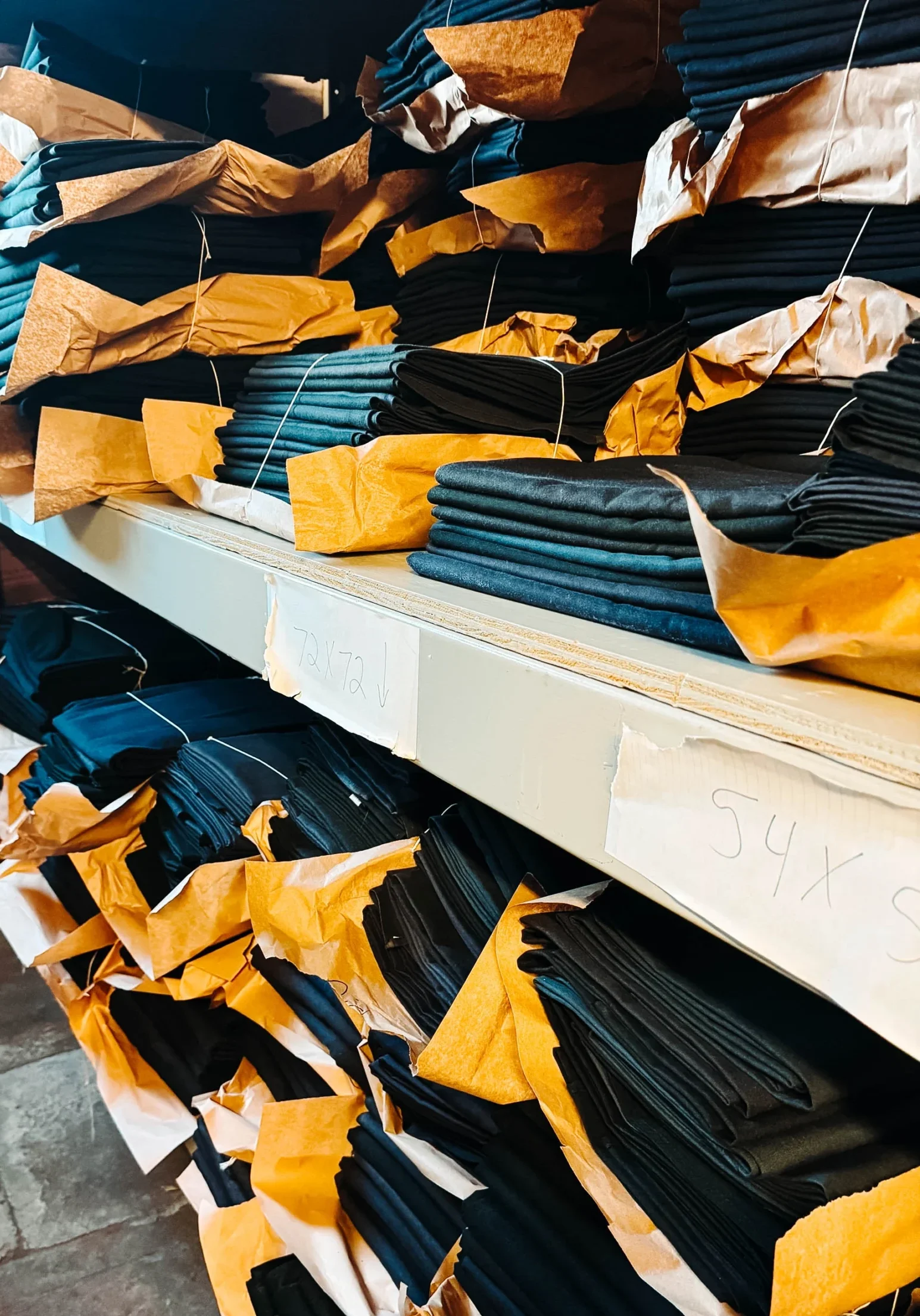 Stacks of folded black linens bundled in kraft paper and organized on industrial shelving in a warehouse