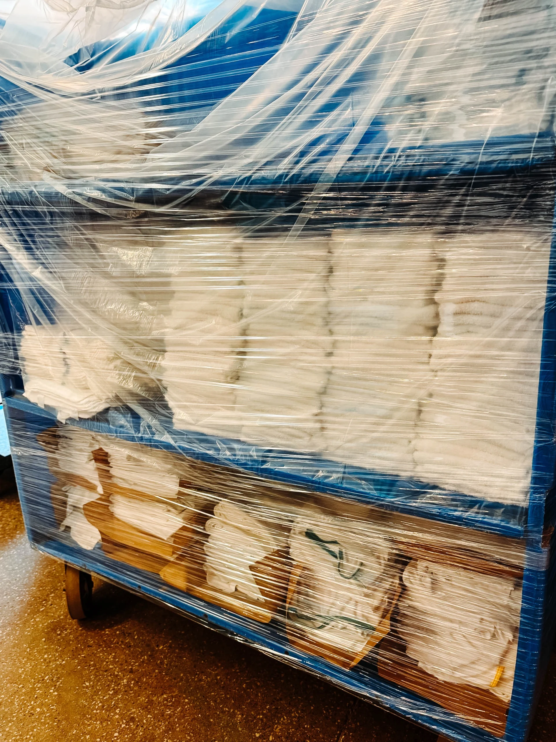 Close-up of a blue industrial linen cart wrapped in plastic containing stacked towels and packaged linens
