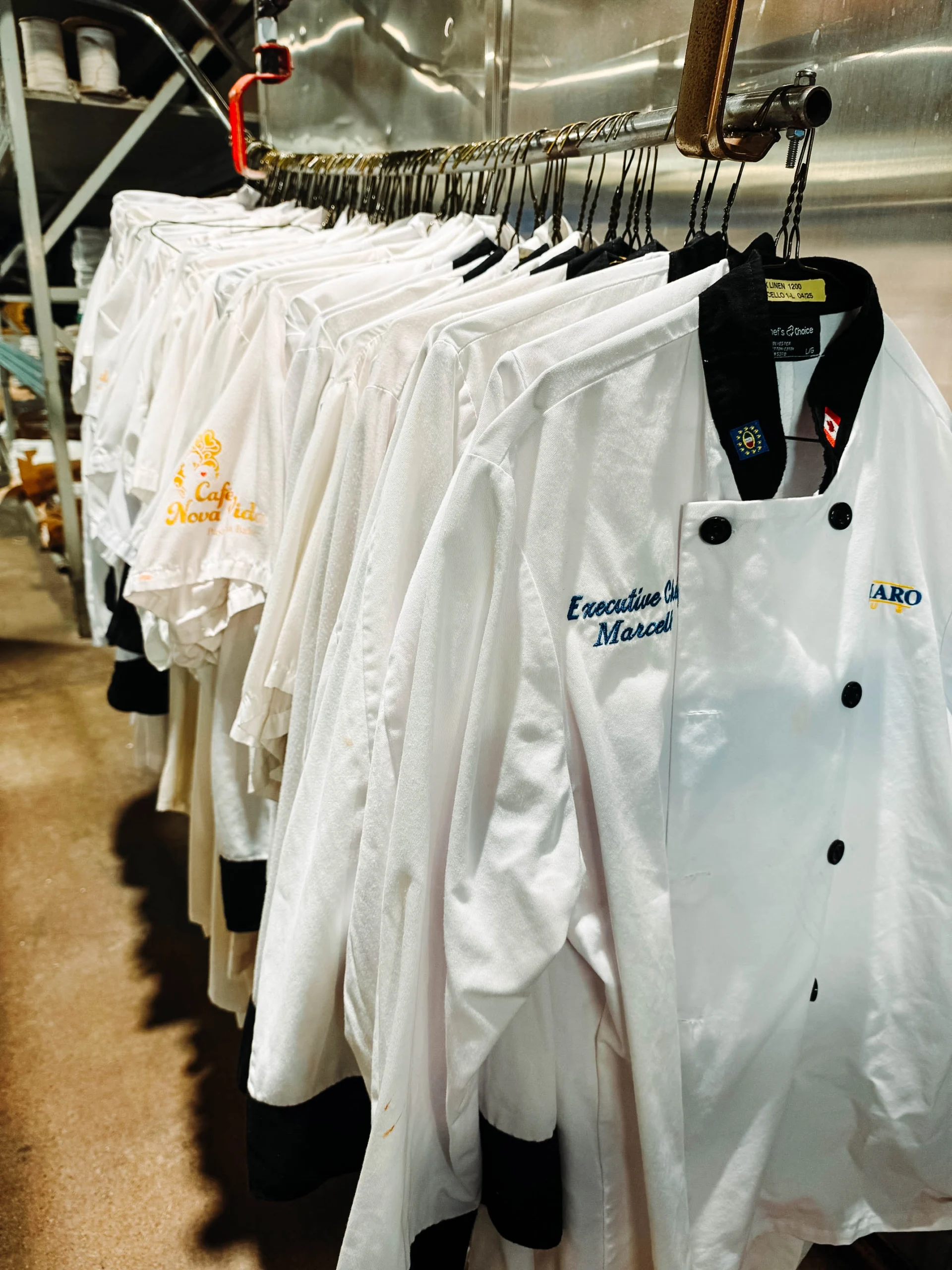 Clean embroidered chef coats hanging in a row on a laundry rack inside a commercial facility